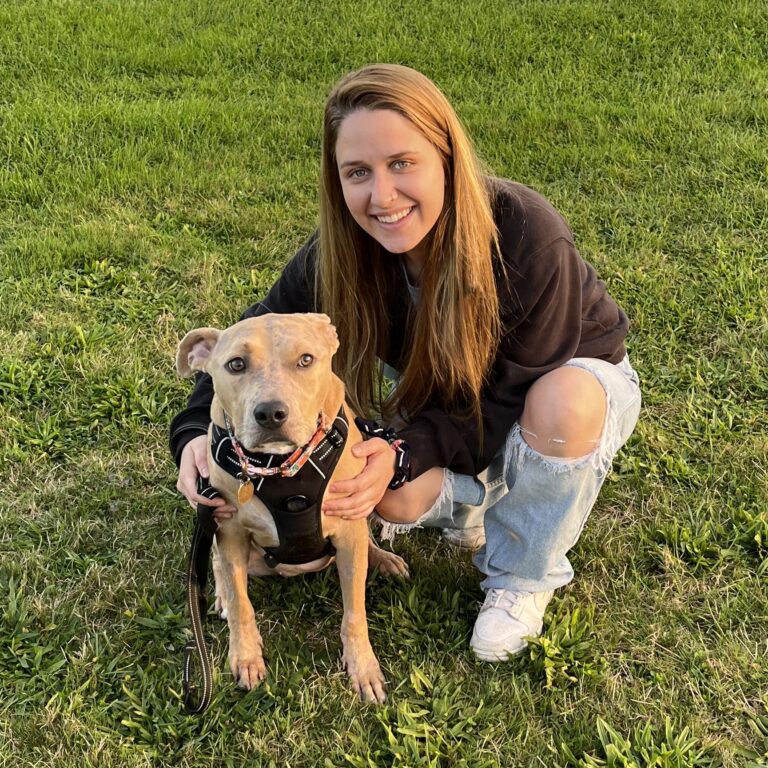 Dr. Duda with a tan, short haired dog, in an outdoor green and grassy area.